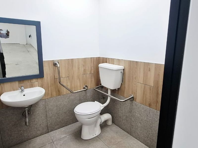 A clean, accessible bathroom featuring a wall-mounted basin, toilet with grab rails, and modern tiled wall finishes.