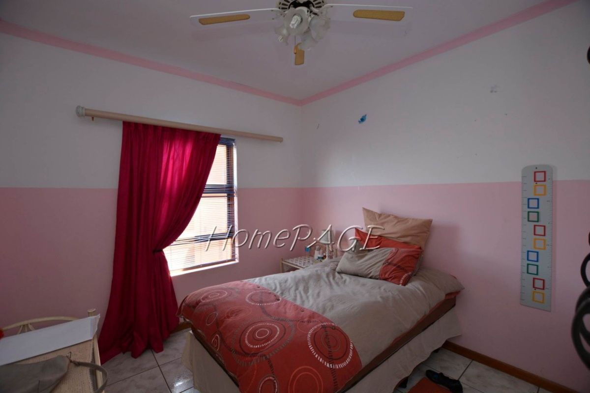 A bedroom featuring tiled flooring, a ceiling fan, and a window with blinds, currently finished with two-tone pink and white wall paint.
