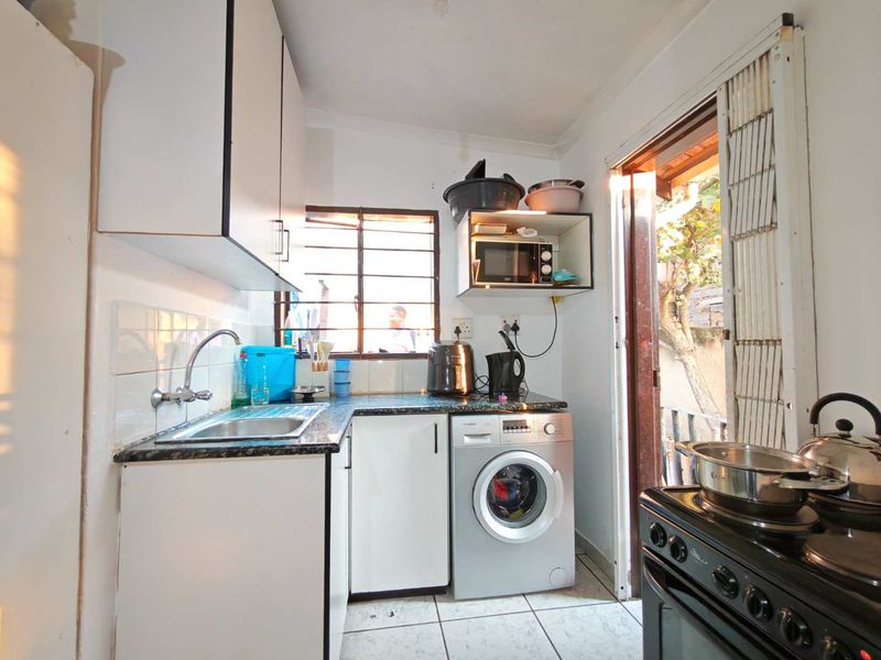 Compact kitchen featuring laminate cabinetry, granite countertops, stainless steel sink, and tiled flooring with direct access to the exterior.