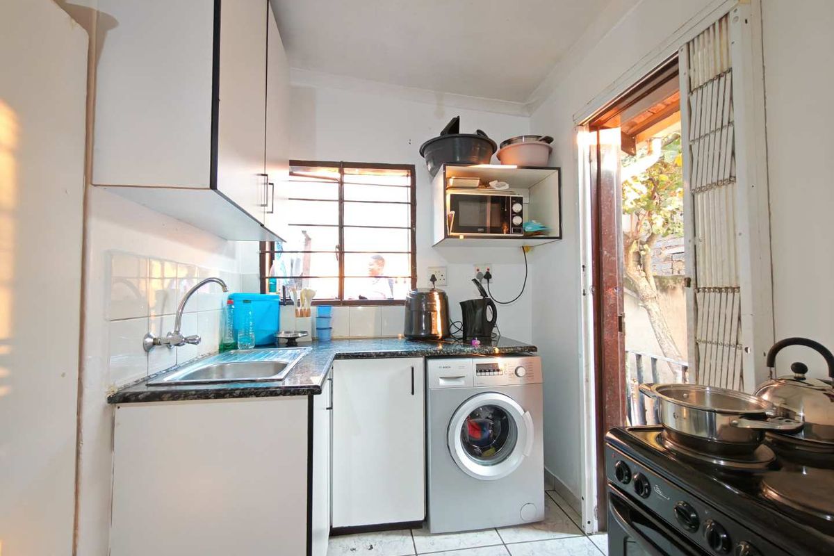 Compact kitchen featuring laminate cabinetry, granite countertops, stainless steel sink, and tiled flooring with direct access to the exterior.