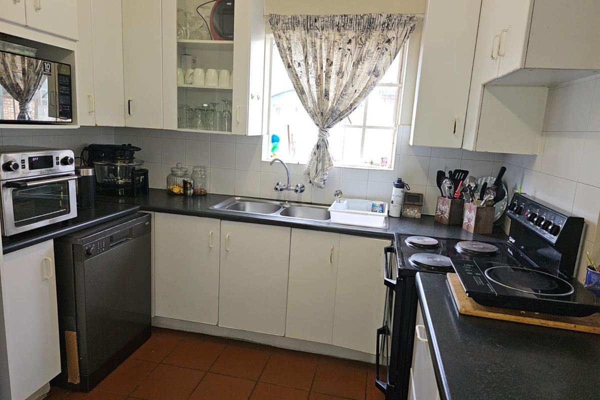 A functional kitchen featuring white cabinetry, dark countertops, a double basin sink, and tiled flooring, providing a practical workspace for daily cooking.