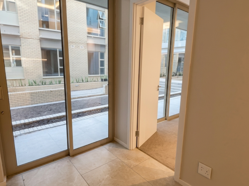 A bright, modern hallway featuring tiled flooring, a sliding glass door leading to an outdoor area, and a doorway connecting to a carpeted room.