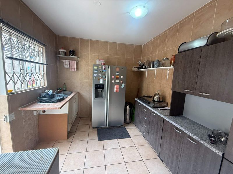 A functional kitchen featuring tiled walls and floors, built-in cabinetry, and a stainless steel sink, with some minor maintenance required for cabinetry.