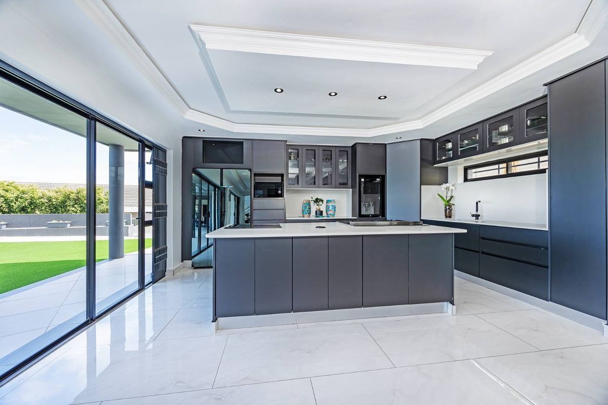 Modern kitchen featuring dark cabinetry, a central island with stone countertops, integrated appliances, and large sliding doors opening to the garden.