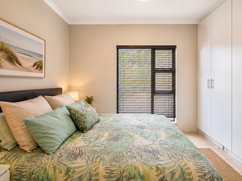 A well-maintained bedroom featuring neutral walls, tiled flooring, built-in cupboards, and dark venetian blinds providing natural light control.