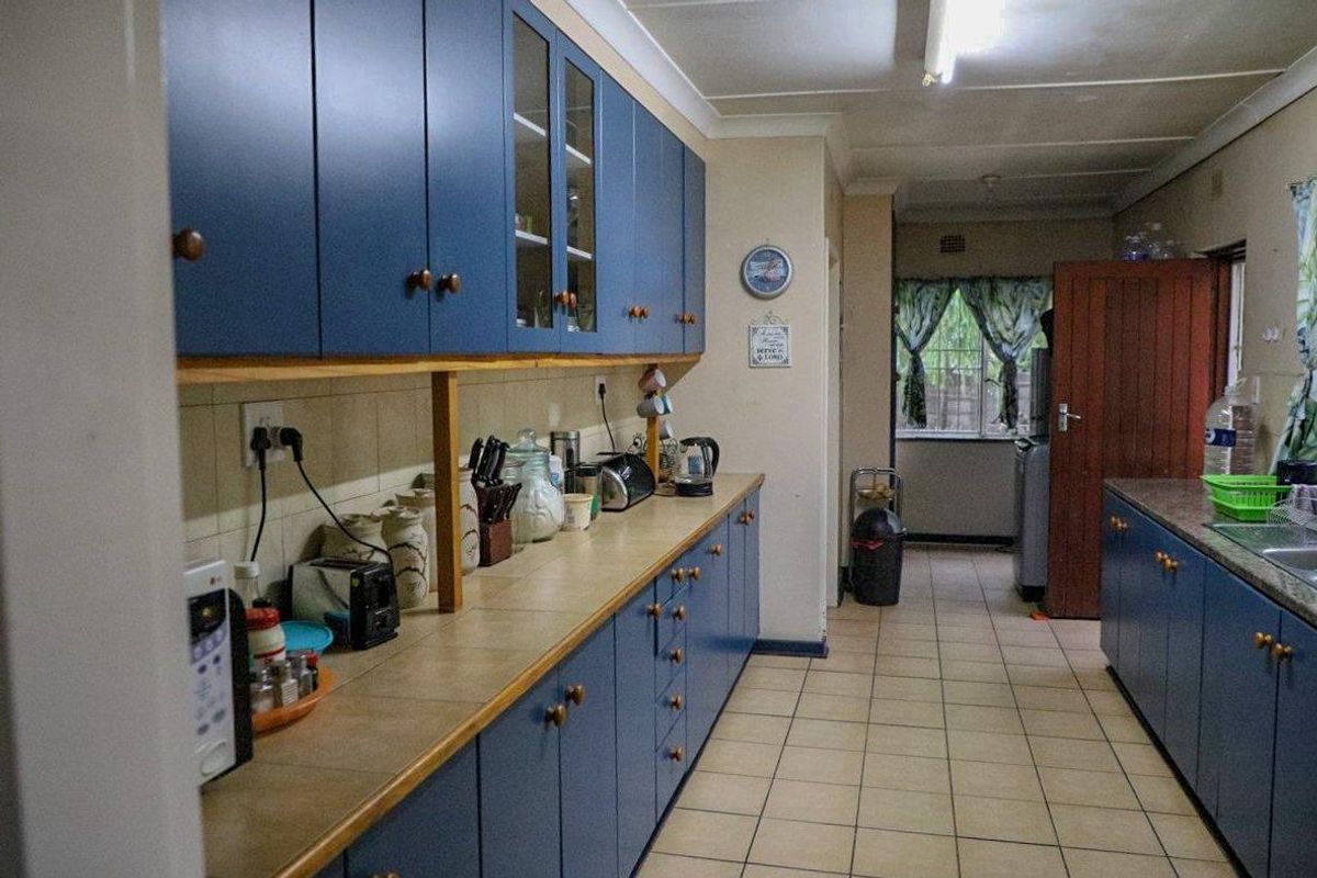 A functional kitchen featuring blue built-in cabinetry, tiled flooring, and ample counter space, leading through to a secondary utility or laundry area.