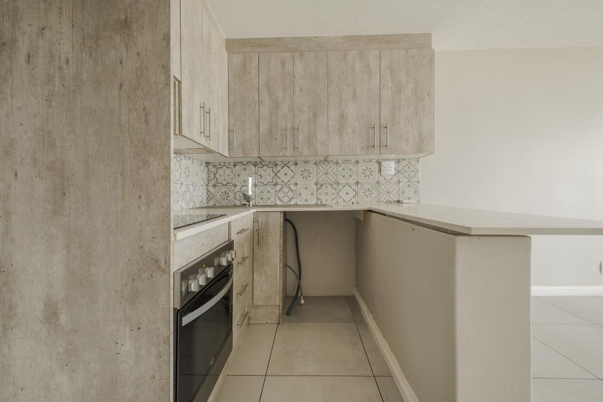 Compact kitchen featuring light wood-look cabinetry, patterned tile backsplash, built-in oven, and a breakfast bar counter with tiled flooring.