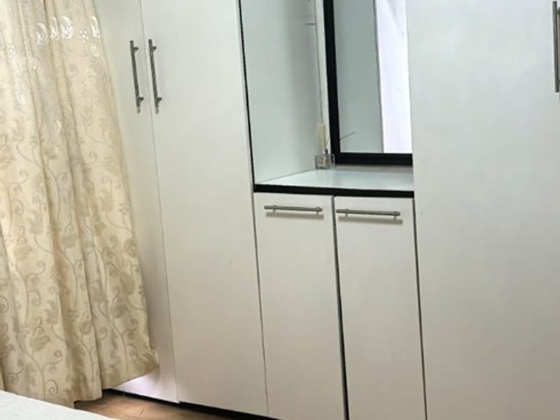 A well-maintained bedroom featuring floor-to-ceiling built-in cupboards with an integrated vanity mirror and warm-toned laminate flooring.