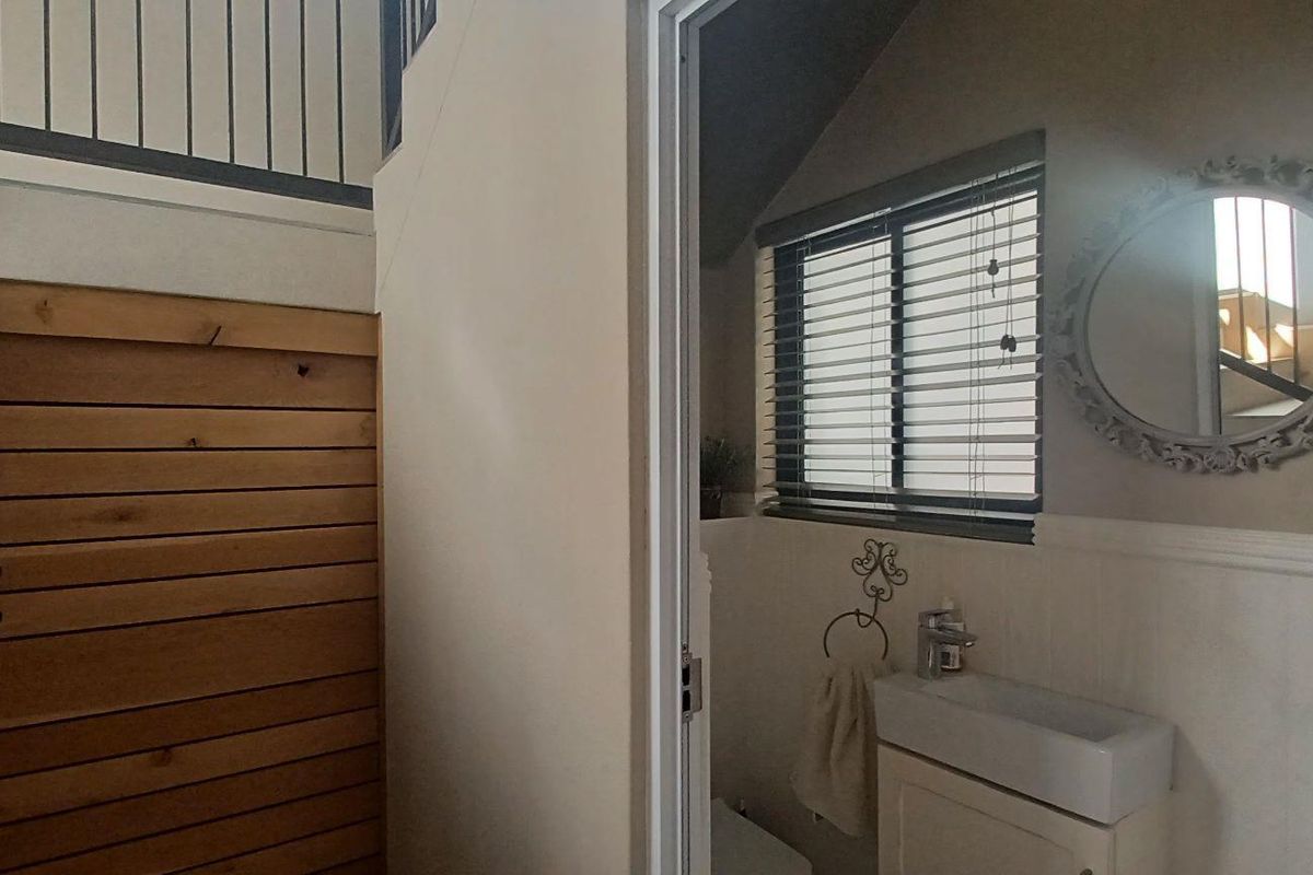 A view of a small bathroom featuring a vanity sink and window, adjacent to a staircase with wooden paneling and integrated storage.