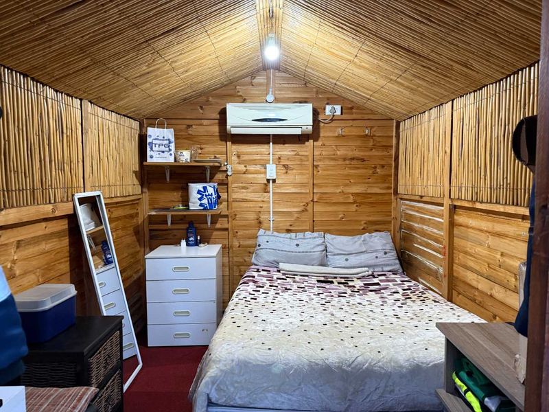 A cozy bedroom featuring timber wall cladding, a bamboo ceiling, and a wall-mounted split-system air conditioner.
