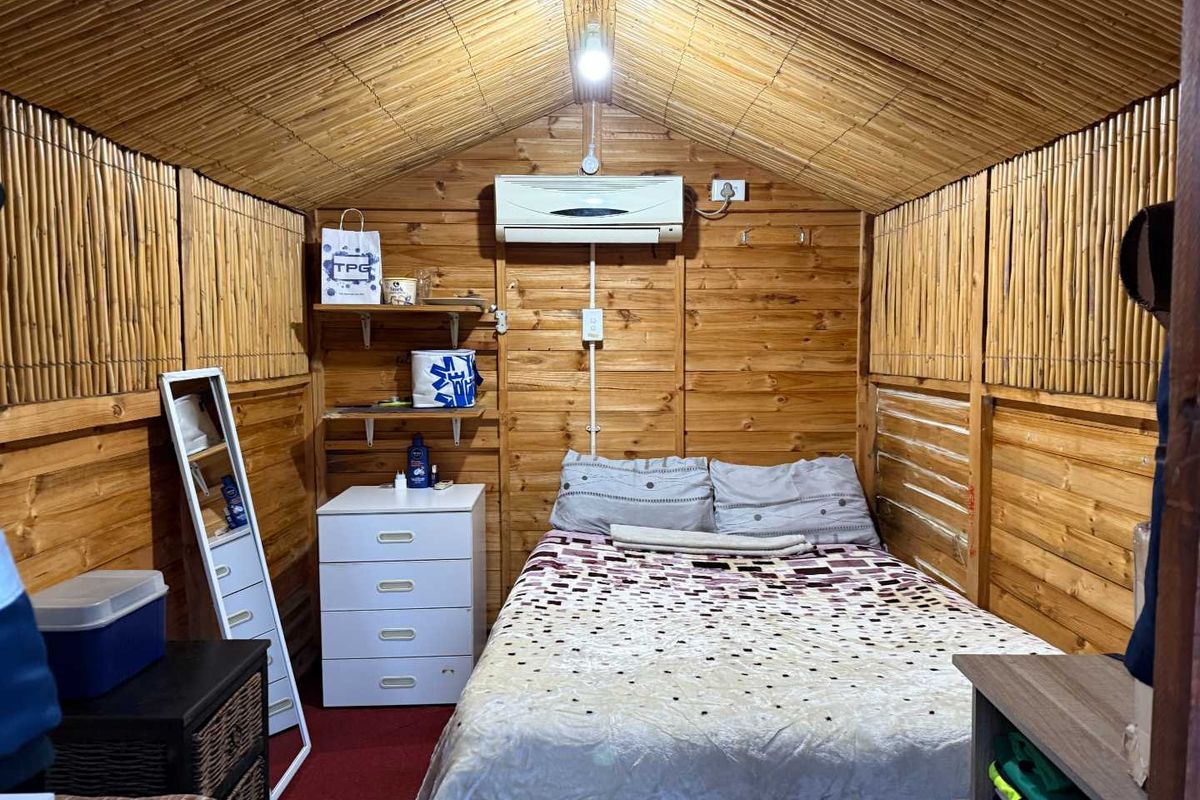 A cozy bedroom featuring timber wall cladding, a bamboo ceiling, and a wall-mounted split-system air conditioner.