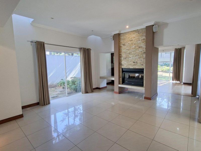 Spacious living area featuring large format floor tiles, a central stone-clad fireplace, and sliding doors providing access to the garden.