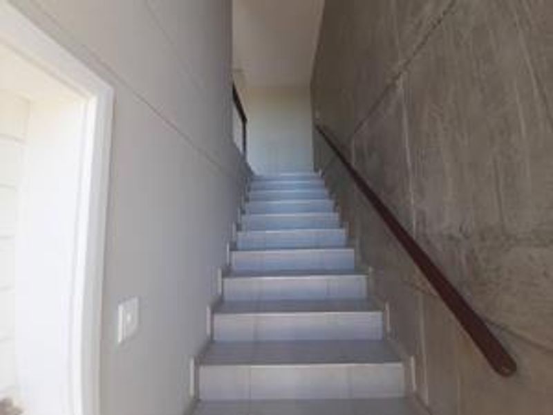 A clean, modern staircase featuring tiled steps, a wooden handrail, and a striking exposed concrete feature wall.