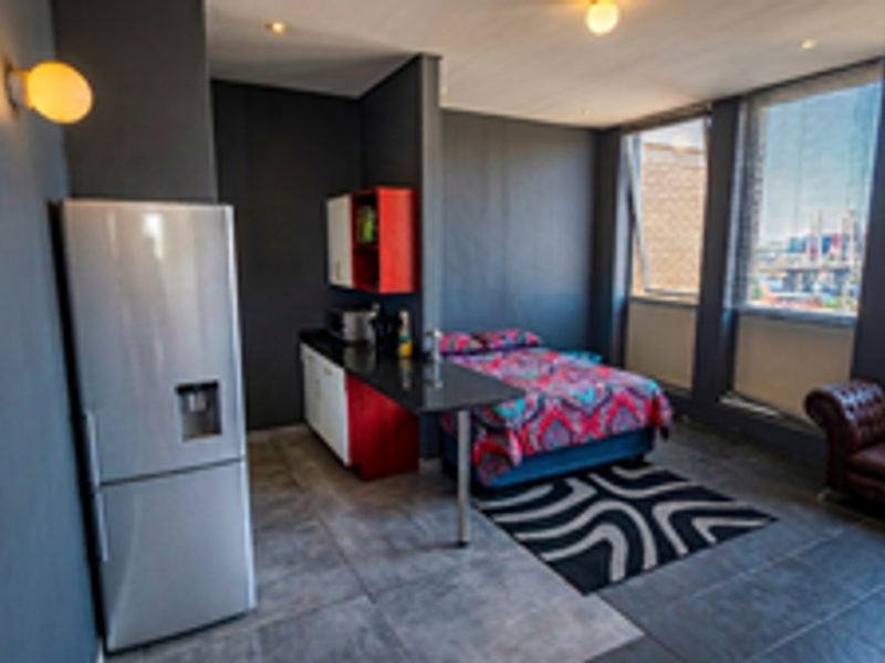 Open-plan studio apartment featuring a compact kitchenette, tiled flooring, and large windows providing natural light and urban views.