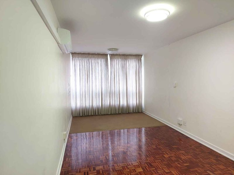An empty living room featuring classic parquet flooring, a wall-mounted split-system air conditioner, and neutral walls, ready for personalization.