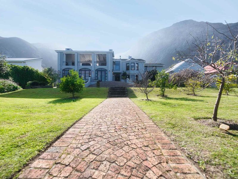 A spacious rear garden featuring a cobblestone pathway leading to a multi-level residence with large glass windows and mountain views.