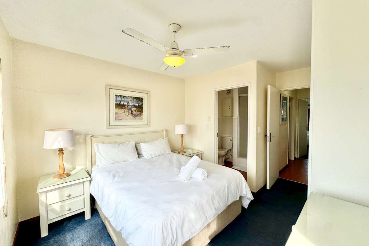 A bedroom featuring a ceiling fan, en-suite bathroom access, and neutral wall finishes, providing a functional and comfortable living space.
