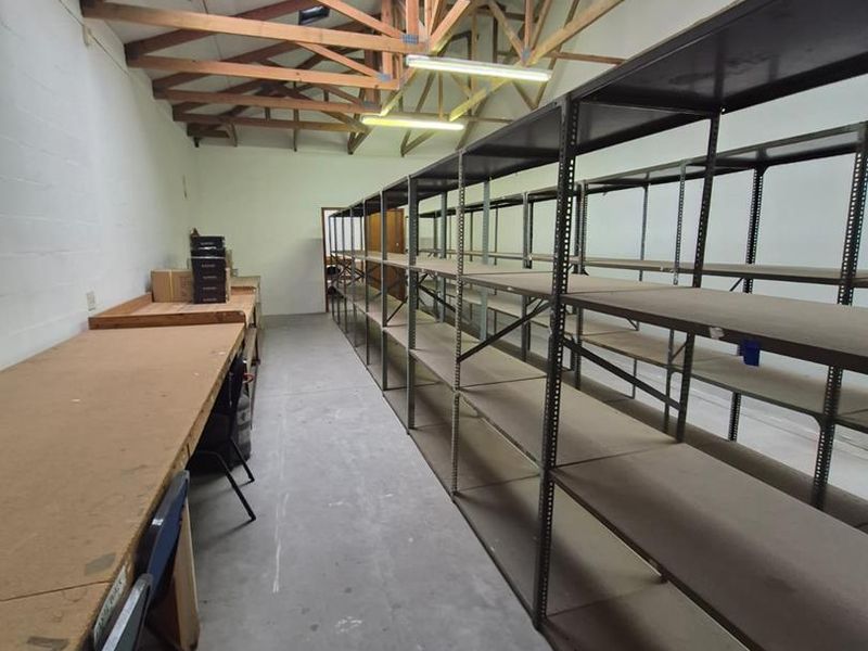 A functional utility or storage space featuring exposed timber roof trusses, a skylight, concrete flooring, and extensive built-in metal shelving units.