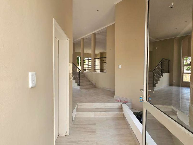 Spacious entrance hall featuring light-toned tiled flooring, recessed lighting, and an open-plan staircase with a modern metal balustrade leading to the upper level.