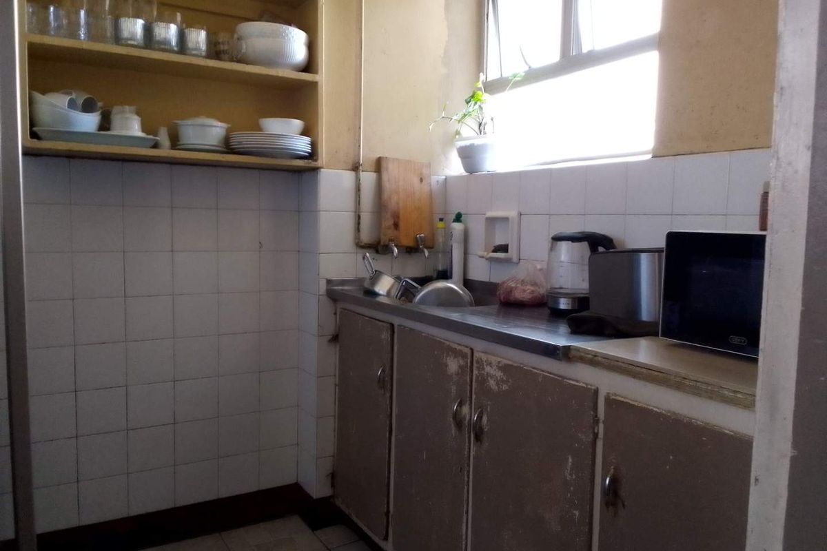 A dated kitchen area featuring a stainless steel sink, built-in cabinetry, and wall-mounted shelving, requiring cosmetic updates and modernization.