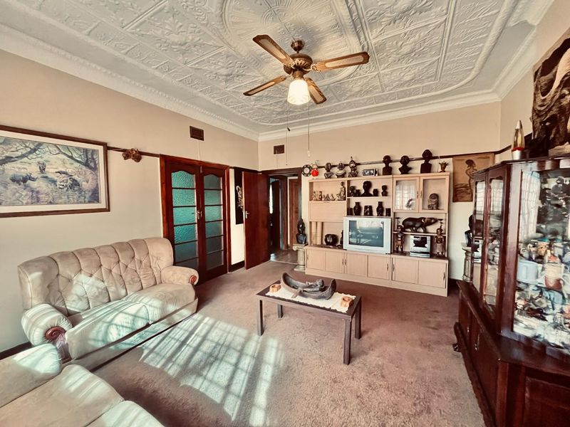 A living room featuring a decorative pressed metal ceiling, ceiling fan, and classic timber door frames, offering a traditional aesthetic with potential for modernization.