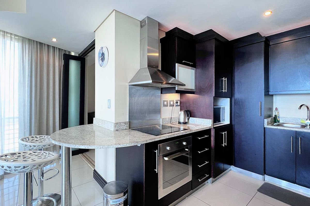 Modern kitchen featuring dark wood cabinetry, granite countertops, a breakfast bar, and integrated stainless steel appliances including an oven and extractor fan.