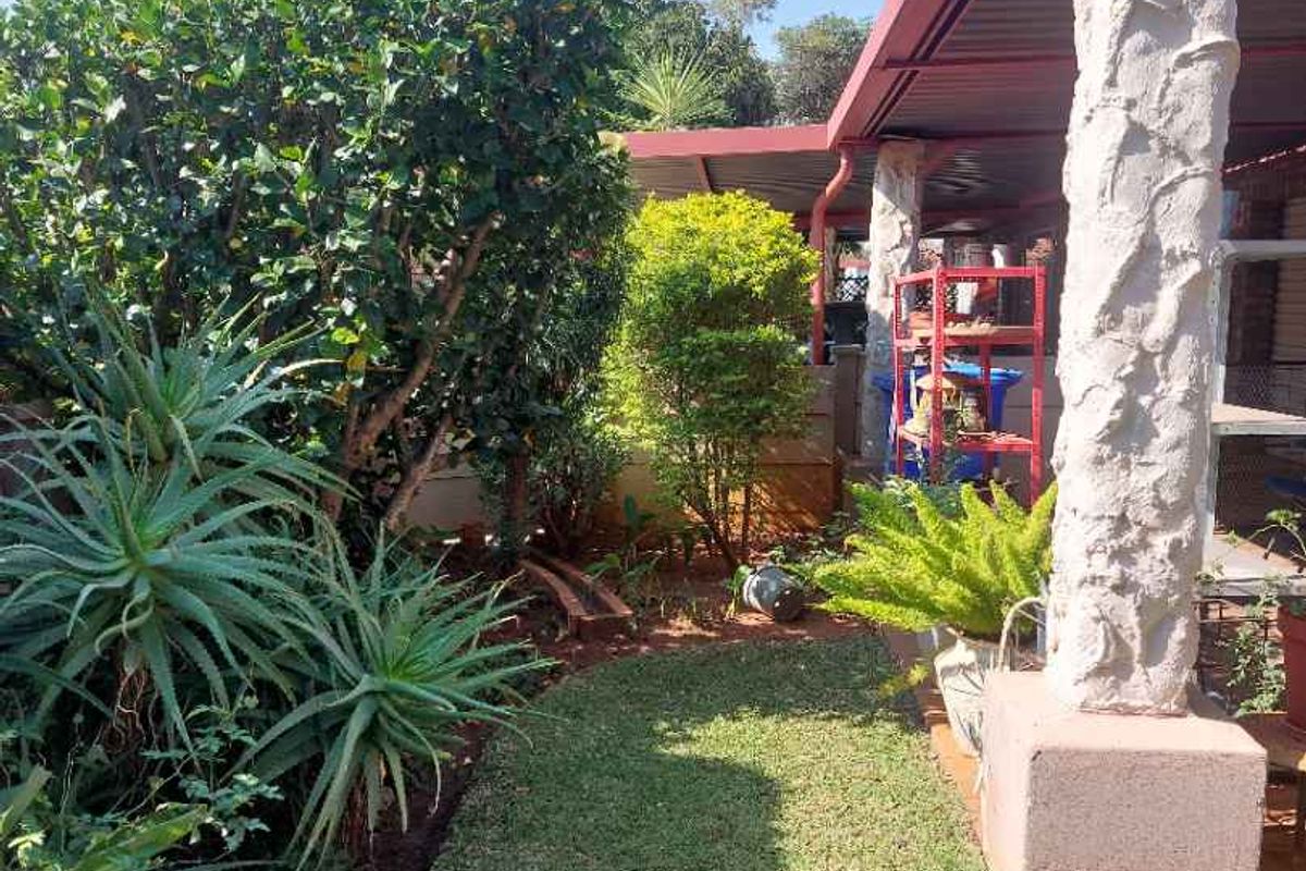A covered patio area featuring a stone-clad support column, overlooking a landscaped garden with established greenery.