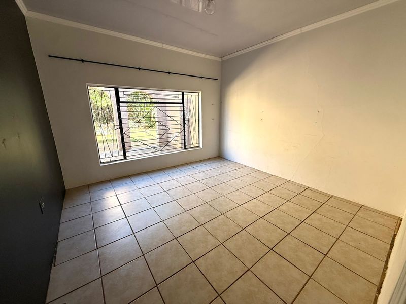 An empty bedroom featuring tiled flooring, security burglar bars on the window, and crown molding, requiring minor wall repairs and cosmetic updates.