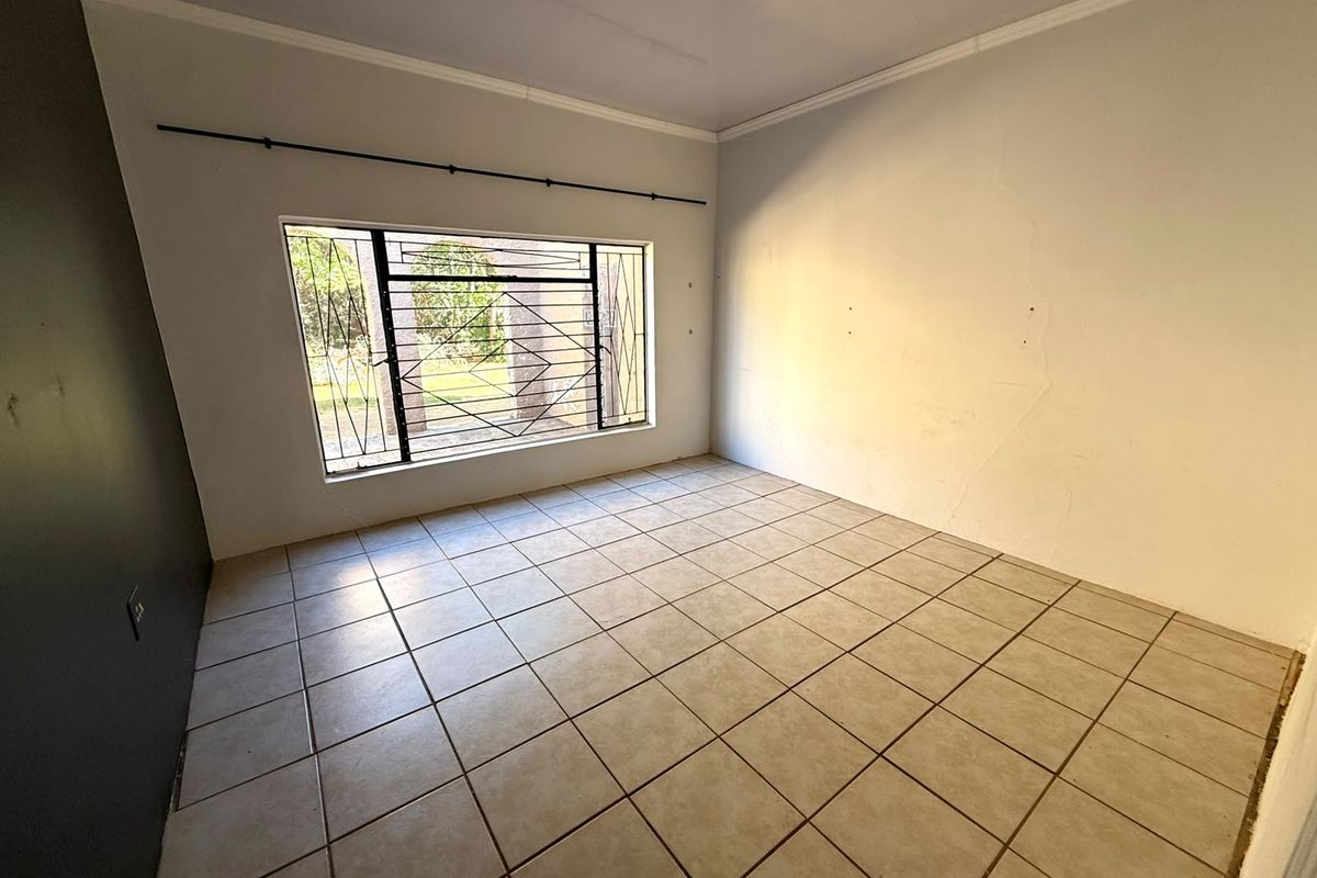 An empty bedroom featuring tiled flooring, security burglar bars on the window, and crown molding, requiring minor wall repairs and cosmetic updates.