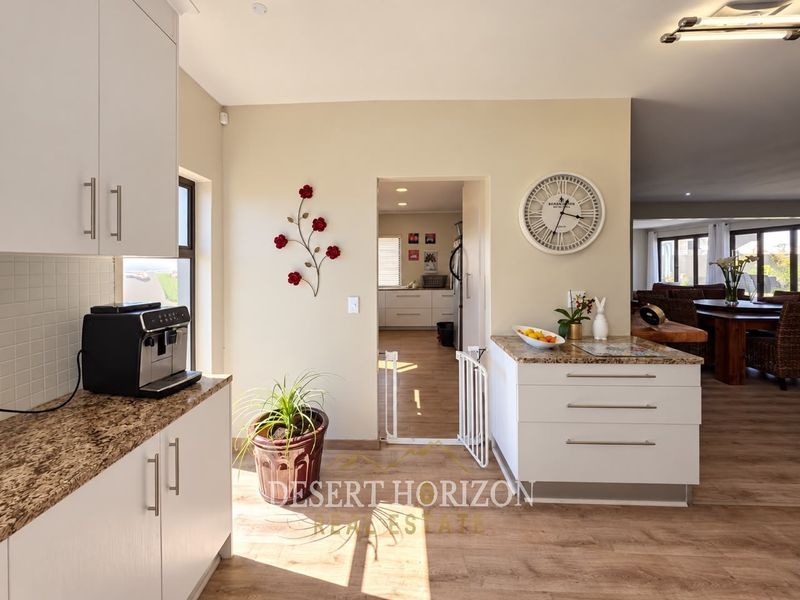 A bright kitchen featuring white cabinetry, granite countertops, and laminate flooring, with an open flow into the adjacent dining and living areas.