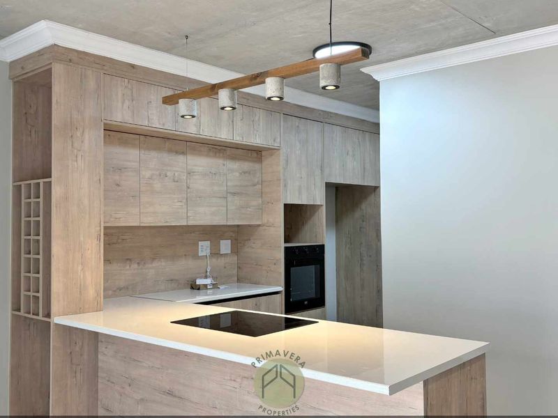 Modern kitchen featuring light wood-grain cabinetry, stone countertops, integrated induction hob, built-in oven, and stylish pendant lighting with a raw concrete ceiling finish.