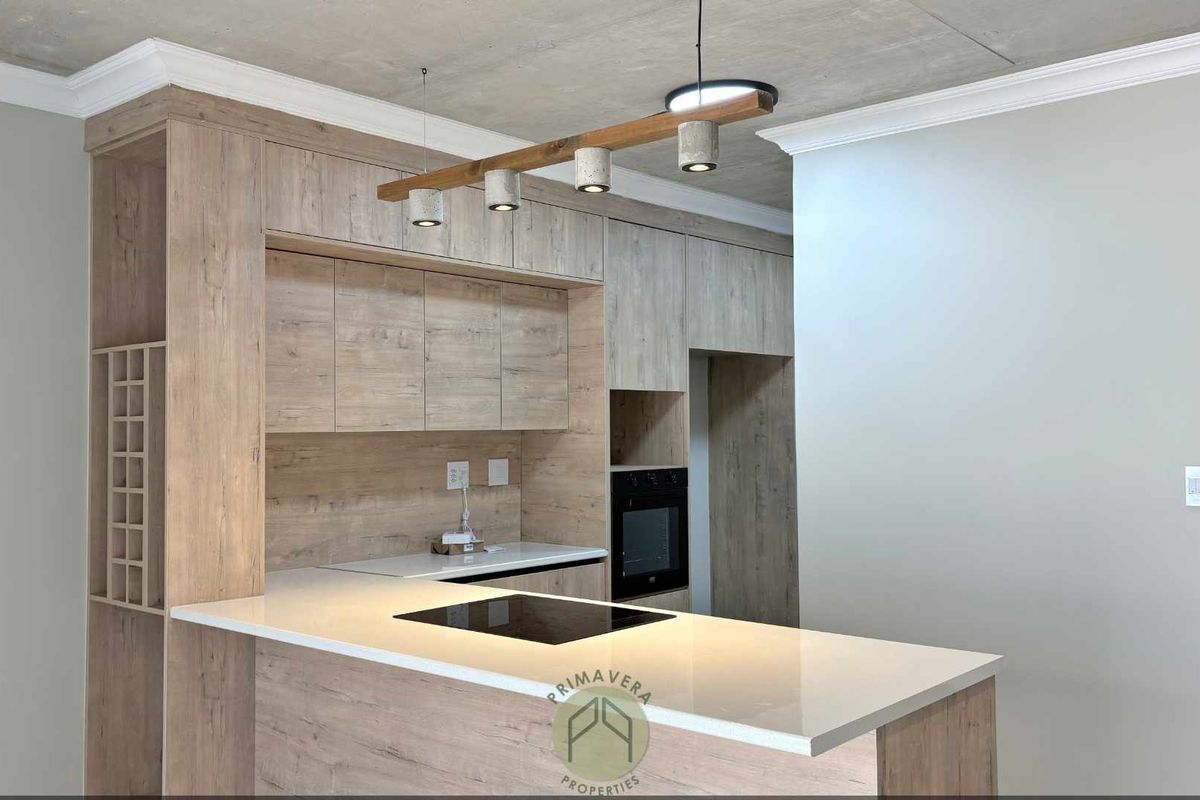 Modern kitchen featuring light wood-grain cabinetry, stone countertops, integrated induction hob, built-in oven, and stylish pendant lighting with a raw concrete ceiling finish.