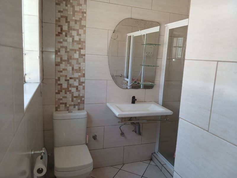 A functional bathroom featuring a wall-mounted basin, toilet, and shower enclosure with neutral wall tiles and a decorative mosaic feature strip.