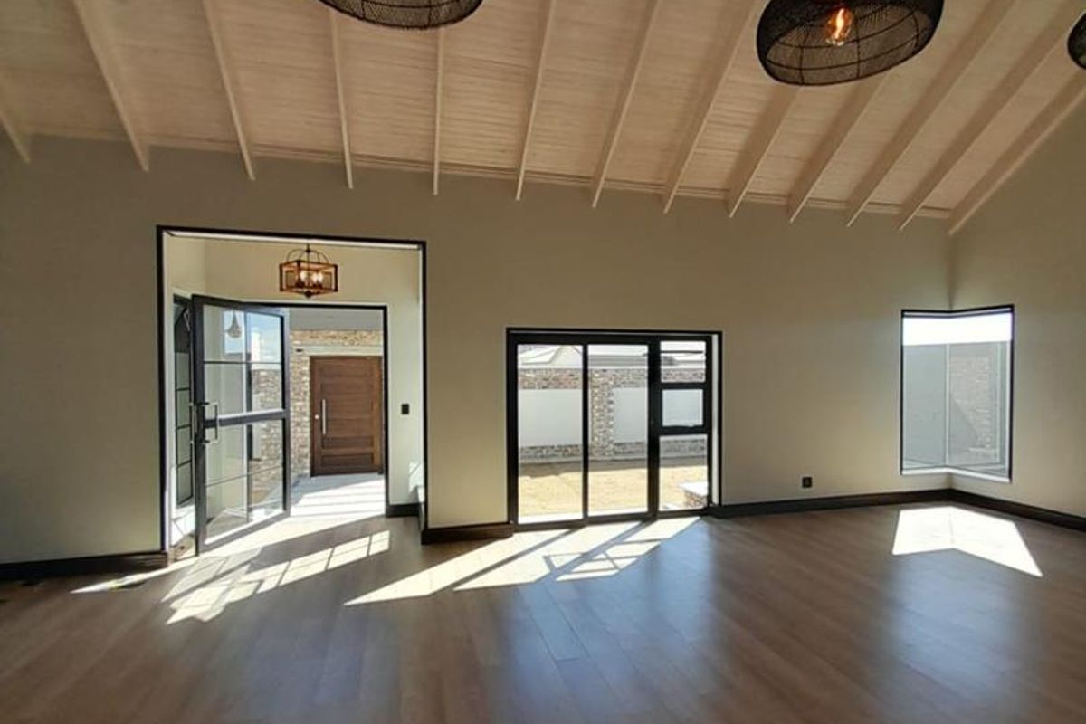 Spacious living area featuring high vaulted ceilings with exposed timber beams, modern wood-look flooring, and large black-framed windows and doors providing natural light.