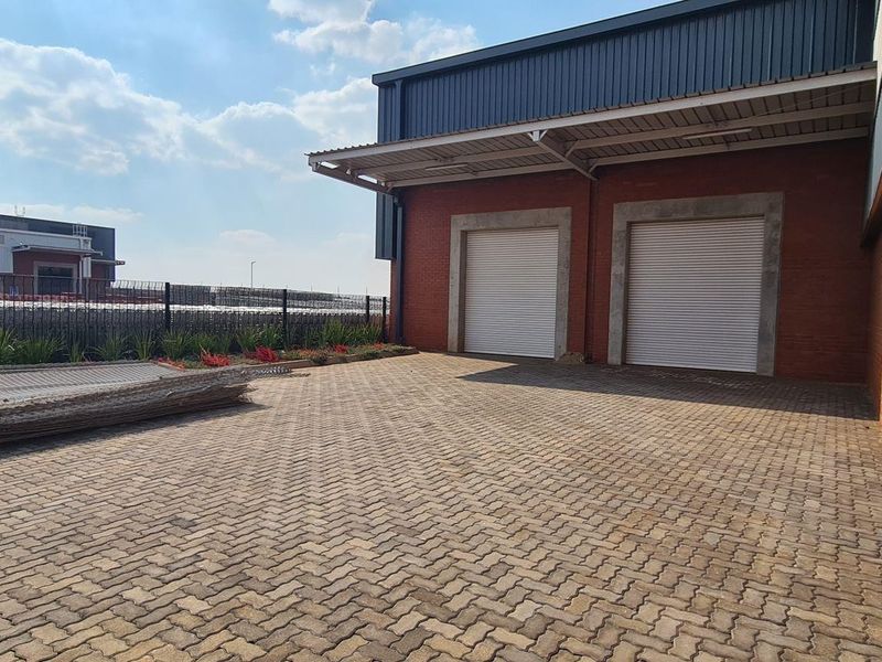 Industrial rear yard featuring paved access, two roller shutter doors, and durable brick and metal construction.