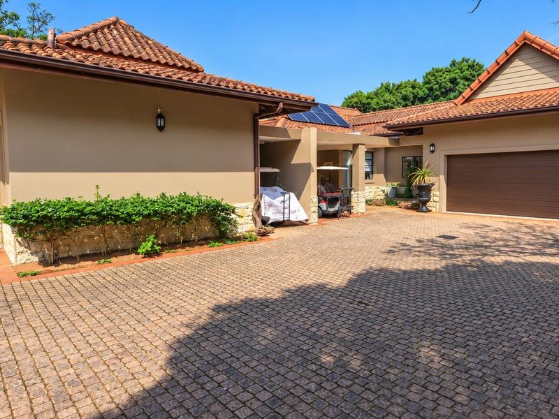 Front exterior view of the house featuring a paved driveway, terracotta roof tiles, solar panels, and a garage.