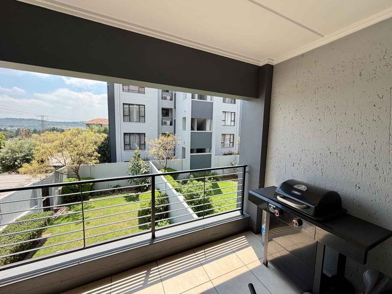 A covered balcony featuring tiled flooring, a metal balustrade, and views over the complex garden and surrounding area.