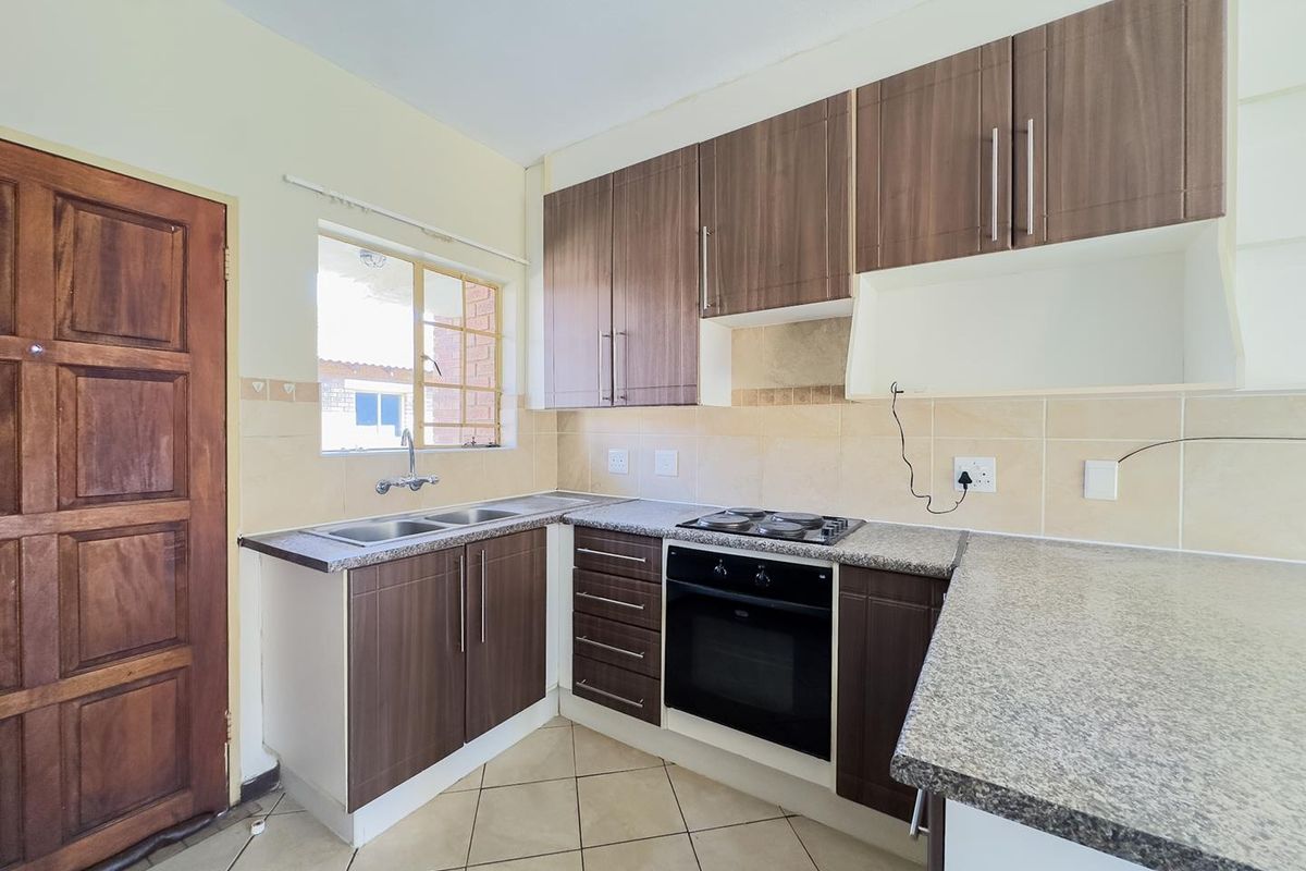 A functional kitchen featuring wood-finish cabinetry, granite countertops, a built-in oven with hob, and tiled flooring, offering a clean and practical workspace.
