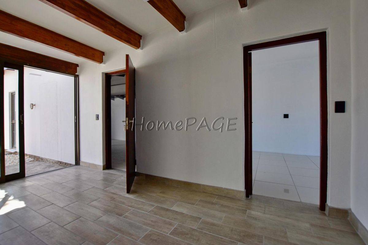 Interior view of a living area featuring exposed timber ceiling beams, tiled flooring, and access to an outdoor patio through glass sliding doors.