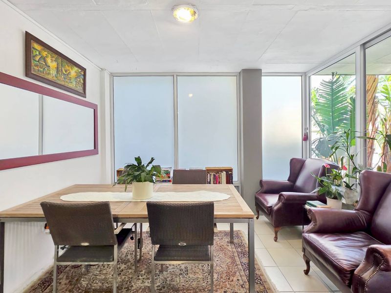 A bright living area featuring large glass windows, tiled flooring, and a neutral color palette, offering a versatile space for dining or relaxation.