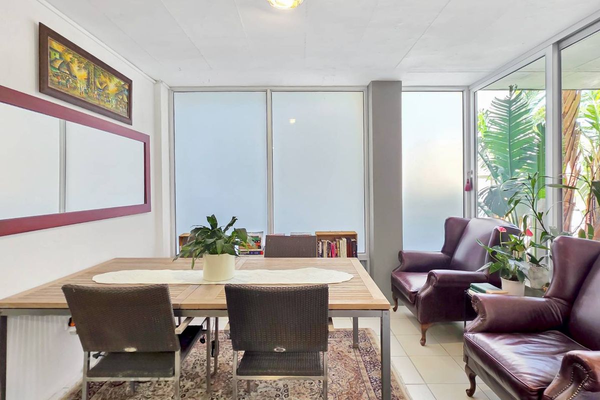 A bright living area featuring large glass windows, tiled flooring, and a neutral color palette, offering a versatile space for dining or relaxation.