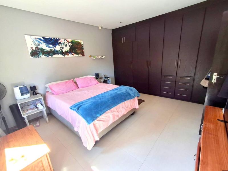 Spacious bedroom featuring extensive dark wood built-in cupboards and neutral tiled flooring, offering ample storage and a clean, functional layout.