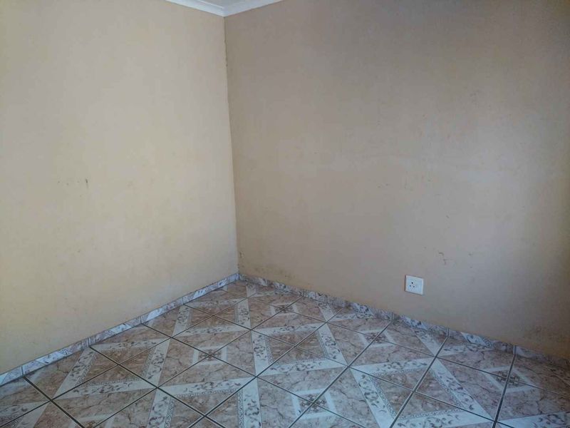 An empty bedroom featuring neutral wall paint and patterned ceramic floor tiles, providing a blank canvas for personalization.