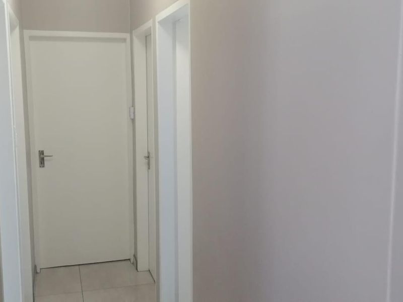 A clean and neutral hallway featuring tiled flooring and multiple internal doors providing access to various rooms.