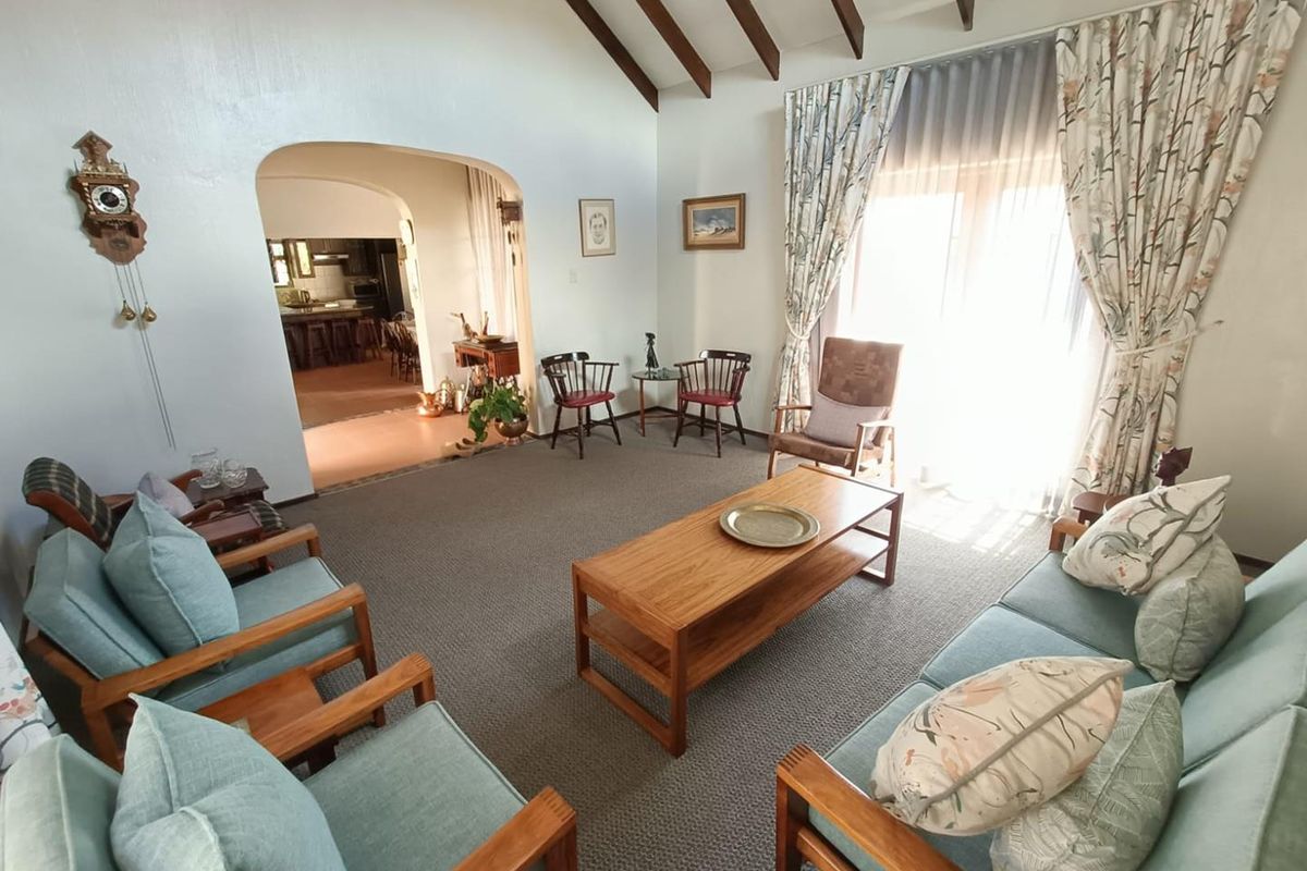 Spacious living room featuring high vaulted ceilings with exposed timber beams, carpeted flooring, and an arched entryway leading to the kitchen area.