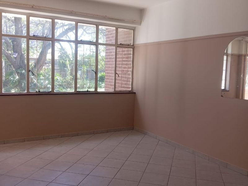 A vacant living area featuring tiled flooring, large windows providing natural light, and a built-in wall mirror, ready for renovation or staging.