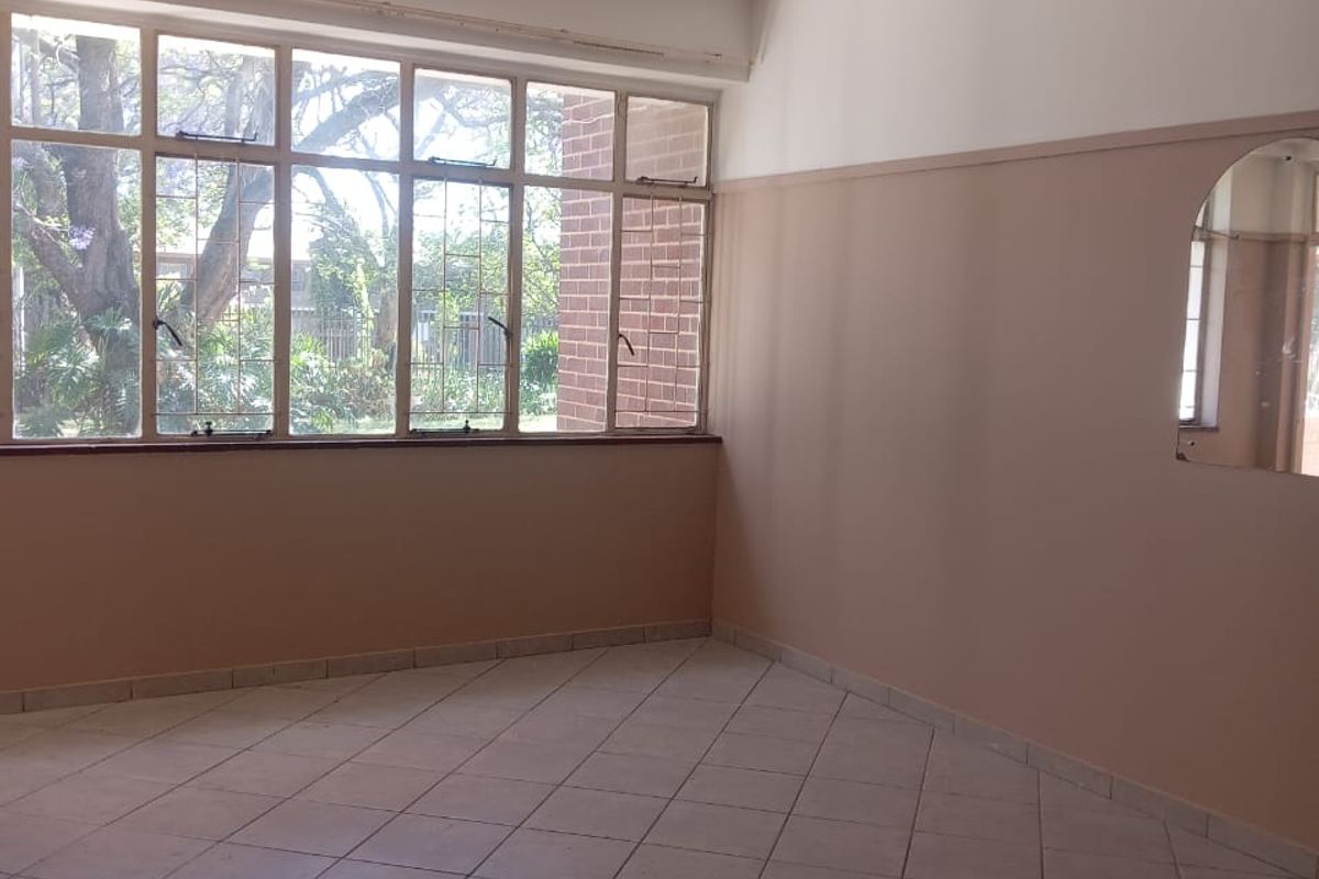 A vacant living area featuring tiled flooring, large windows providing natural light, and a built-in wall mirror, ready for renovation or staging.