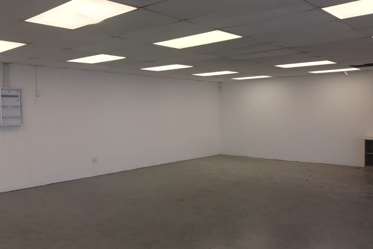 An empty, open-plan commercial space featuring a suspended ceiling with recessed lighting, concrete flooring, and a wall-mounted electrical distribution board.