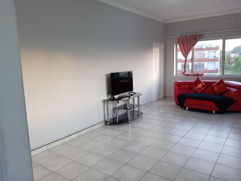 A spacious living area featuring neutral wall finishes, tiled flooring, and a large window providing natural light.