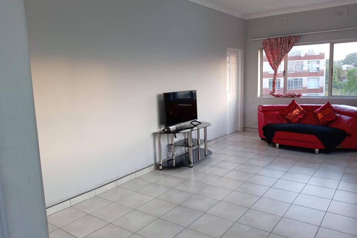 A spacious living area featuring neutral wall finishes, tiled flooring, and a large window providing natural light.